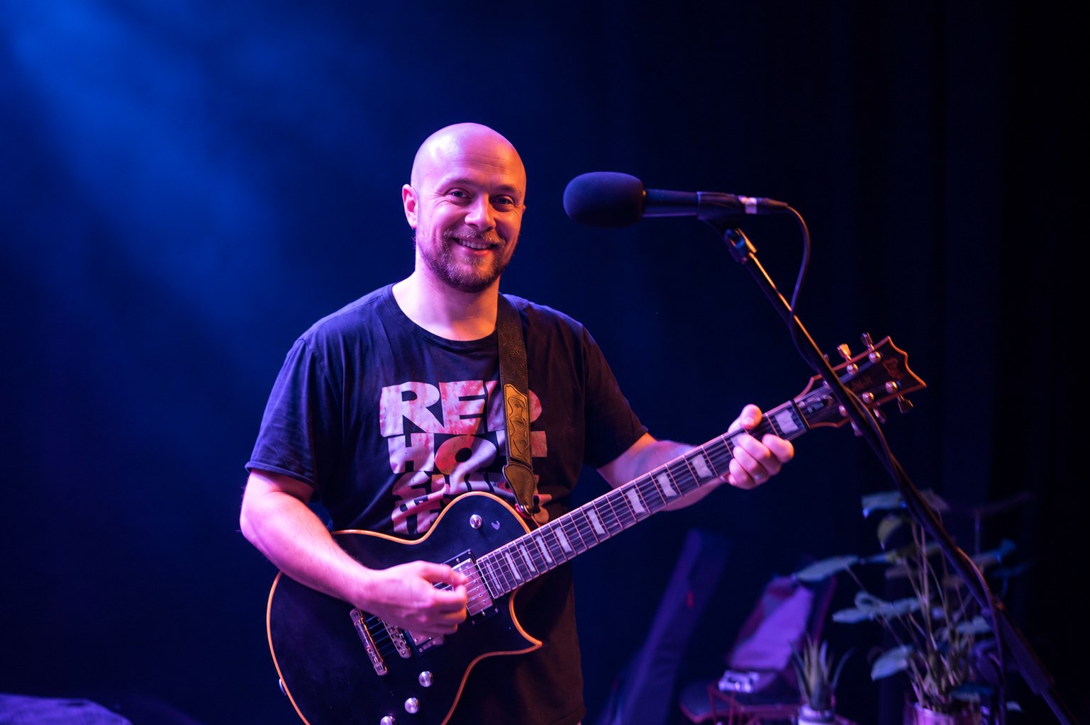 Sunday Service guitarist smiling on stage with an electric guitar.